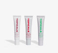 Moisturizing lip balm trio from Topicals Slick Salve in Açaí, Pomegranate, and Mint standing upright side by side on a white background.